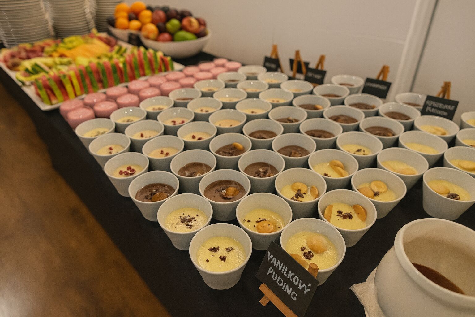Una mesa con varios pequeños recipientes de postres y un cartel que indica 'VANILKOY PUDDING'.