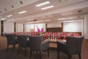 A conference room with rows of red chairs, a long table, and a ceiling with recessed lighting. - Hotel Bratislava (Bratislava)
