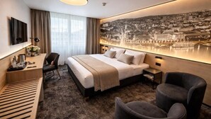 A hotel room with a bed, a desk, a chair, a sofa, and a large cityscape mural on the wall. - Hotel Bratislava (Bratislava)
