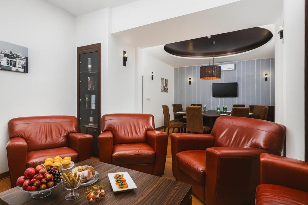 Una sala moderna con sillones de cuero, una mesa de centro de madera con frutas y aperitivos, un comedor con televisor y un diseño de techo original.