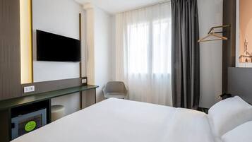 Une chambre d’hôtel équipée d’un lit, d’un bureau, d’une chaise, d’une télévision et d’une fenêtre avec des rideaux.