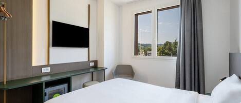 A hotel room with a bed, a desk, a chair, a TV, and a window with curtains.
