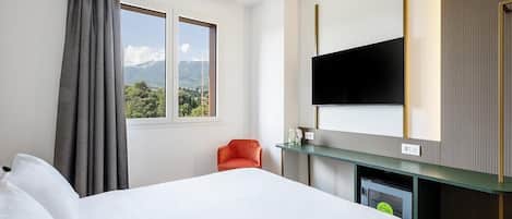 A hotel room with a large bed, a television mounted on the wall, a small table, and a chair.