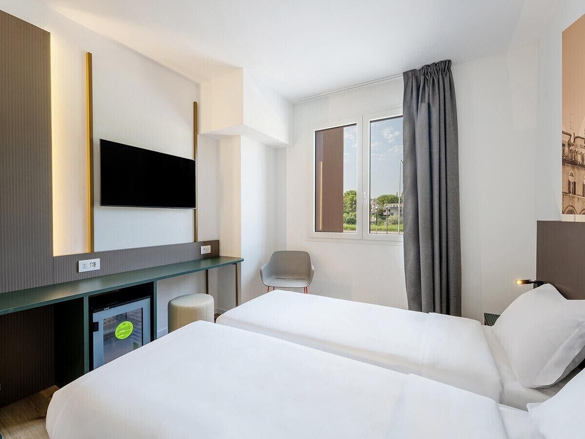 A hotel room with two beds, a desk, a chair, a television, and a window with curtains.