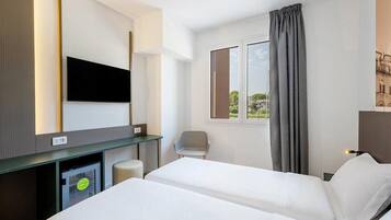 A hotel room with two beds, a desk, a chair, a television, and a window with curtains.