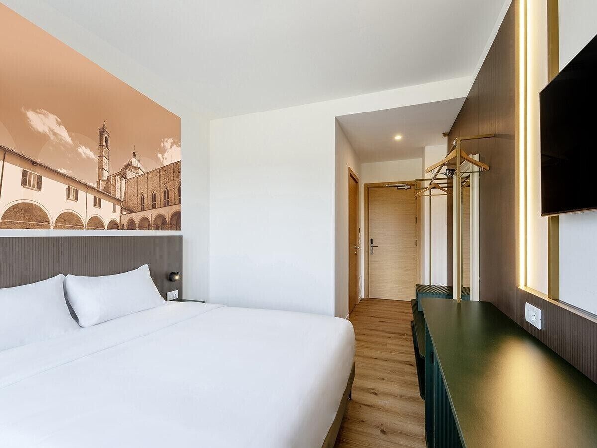 A hotel room with a bed, a wooden floor, a mirror, and a wall-mounted TV.