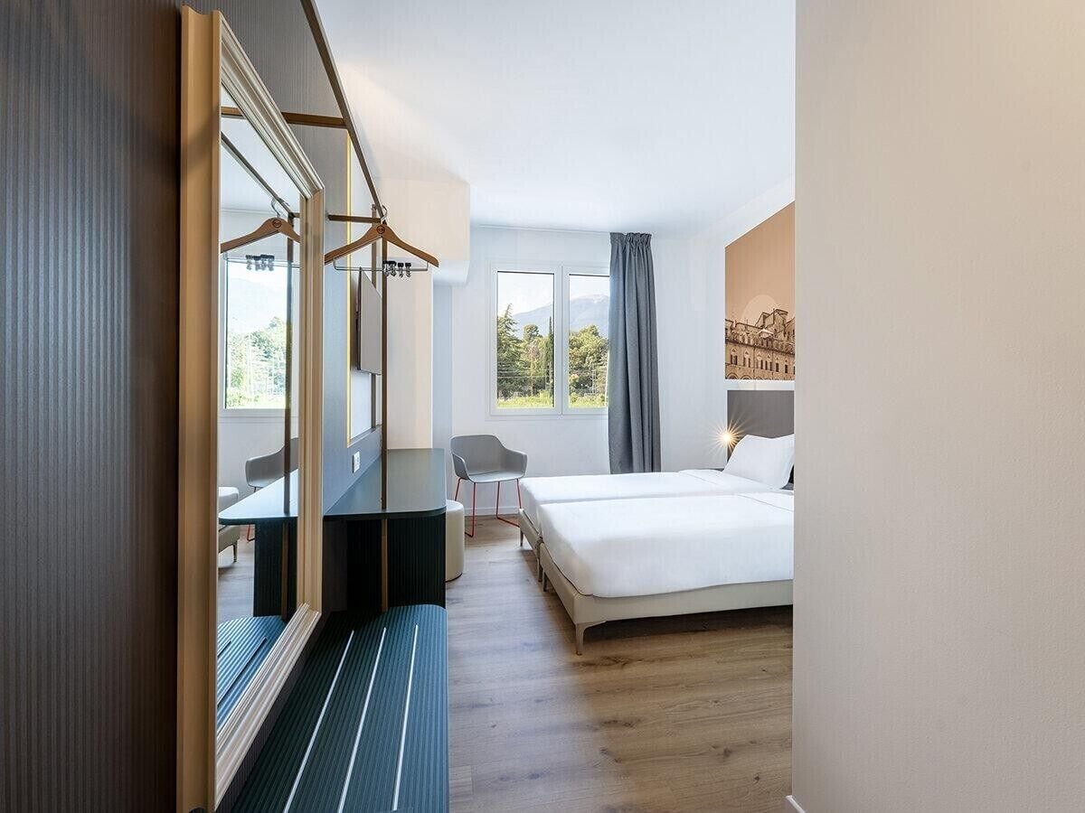 Una habitación de hotel con cama, escritorio, silla y un espejo grande.