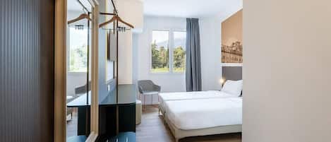 A hotel room with a bed, a desk, a chair, and a large mirror.