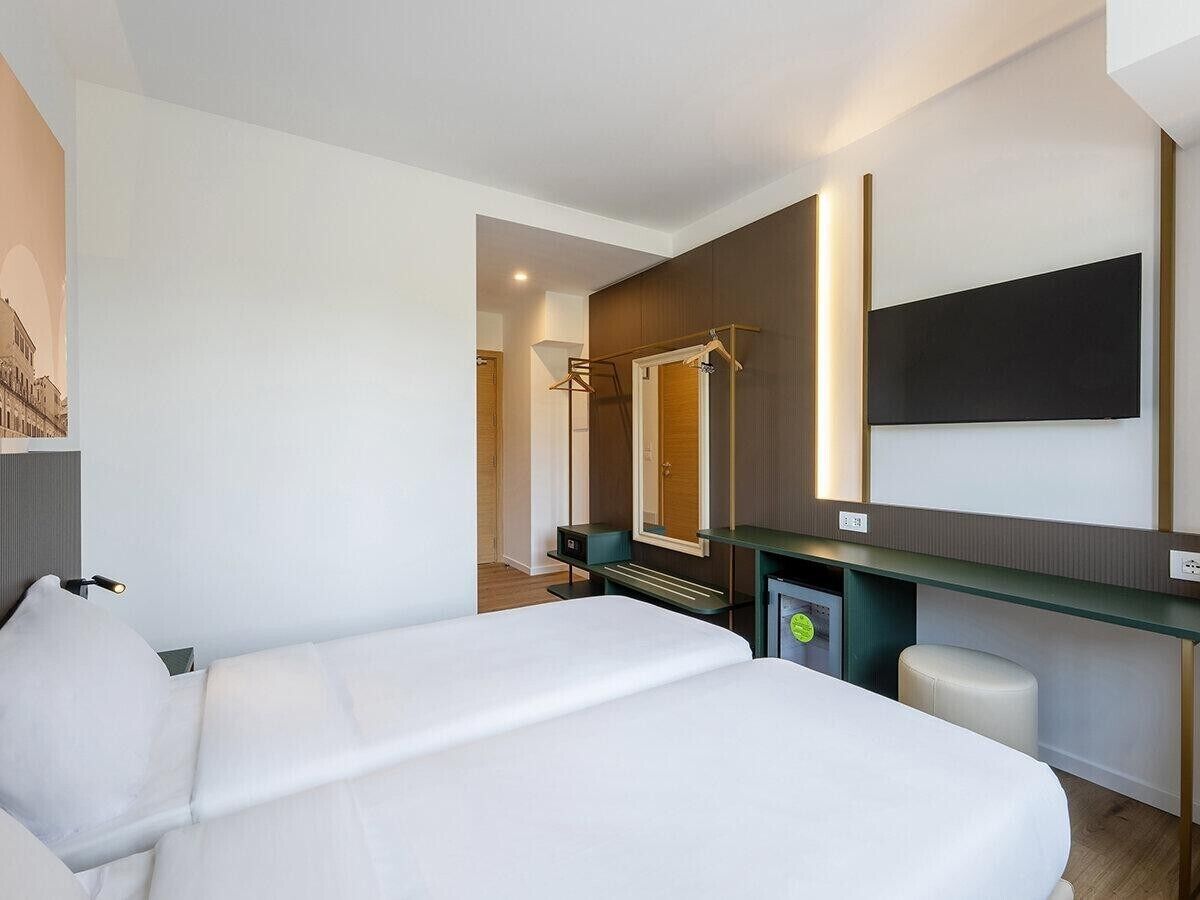 Una camera d'albergo con un letto, una scrivania, uno specchio e una televisione.