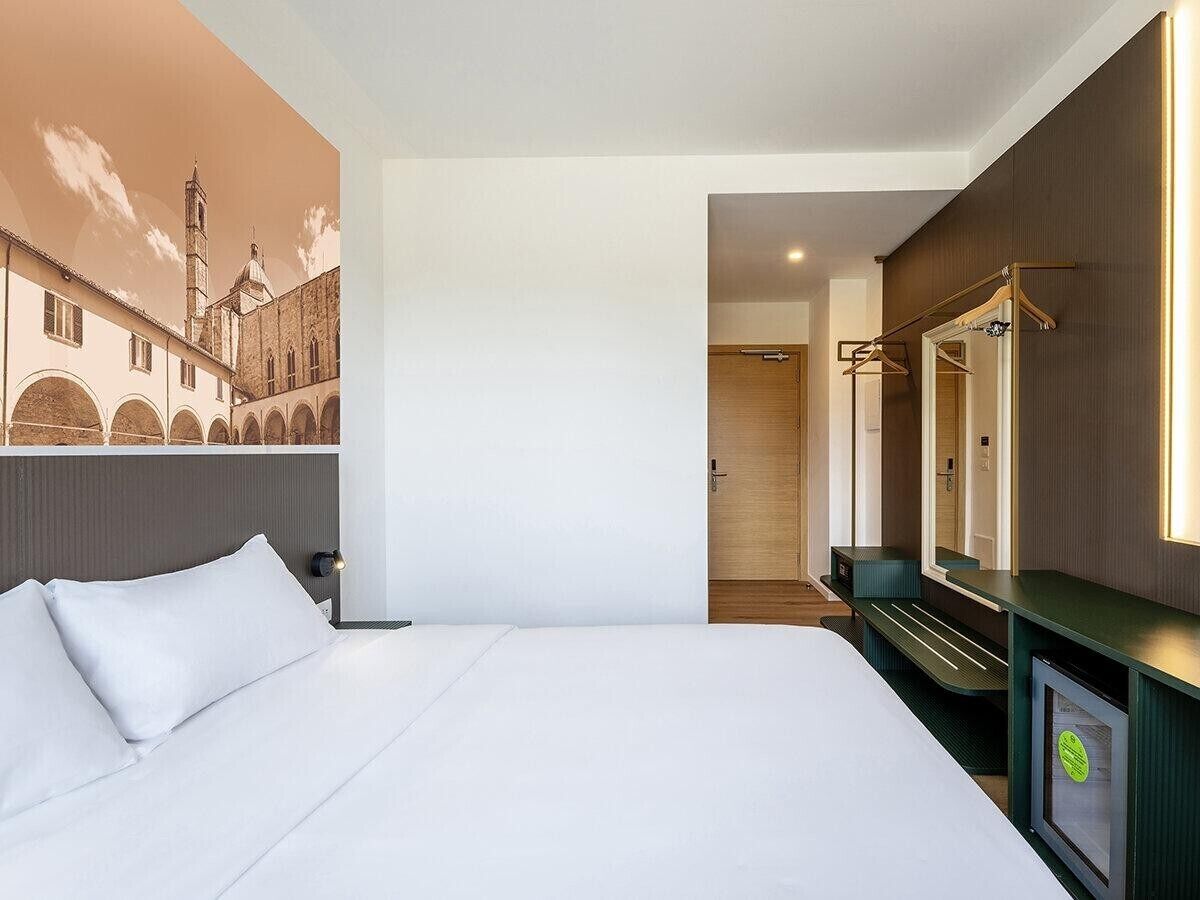Habitación de hotel con cama, espejo, televisor y una pared con un mural.