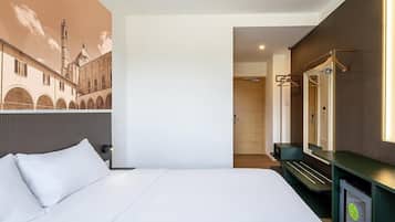A hotel room with a bed, a mirror, a TV, and a wall with a mural.