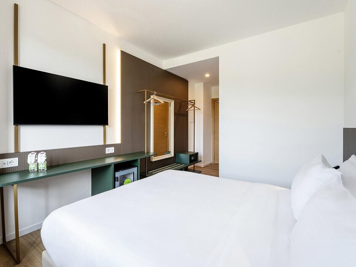 A hotel room with a large bed, a flat-screen TV mounted on the wall, a desk with a mirror, and a wardrobe.