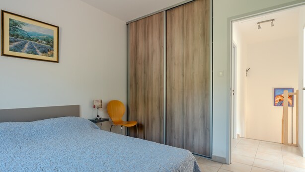 Une chambre à coucher comprenant un lit, une chaise, une armoire et une porte donnant sur une autre pièce.