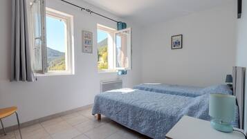 Une chambre avec deux lits, une chaise, un bureau et une fenêtre avec des rideaux.