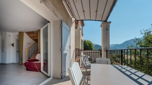 Un balcon avec vue sur les montagnes, un espace couvert avec une table et des chaises, et un escalier menant à une pièce intérieure.