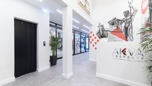 A modern interior with a black elevator, a potted plant, and a wall with a property logo and artwork.