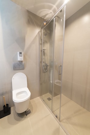 A modern bathroom with a glass-enclosed shower, a toilet, and a soap dispenser.
