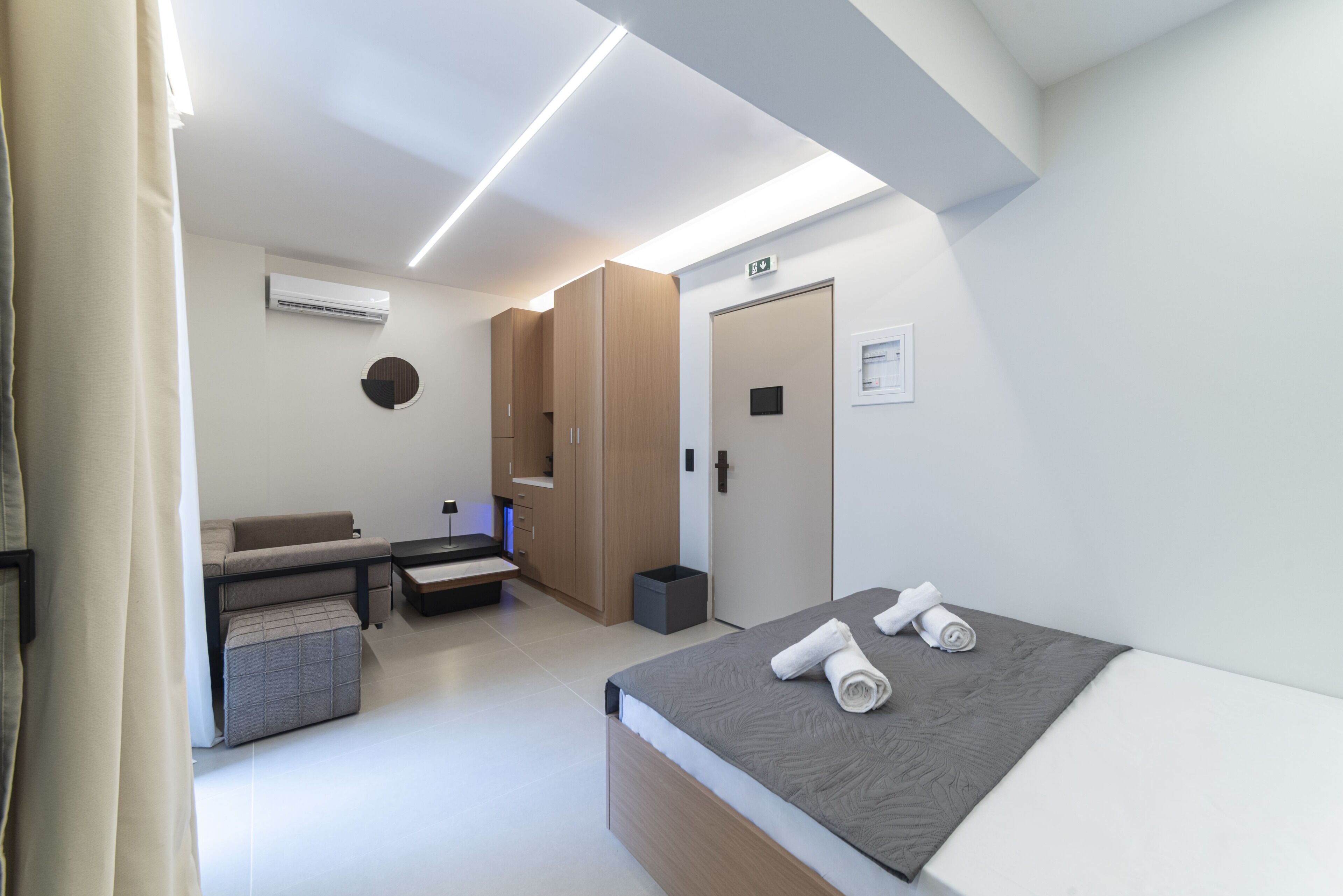 Una habitación de hotel moderna con cama, zona de estar, armario y aire acondicionado.