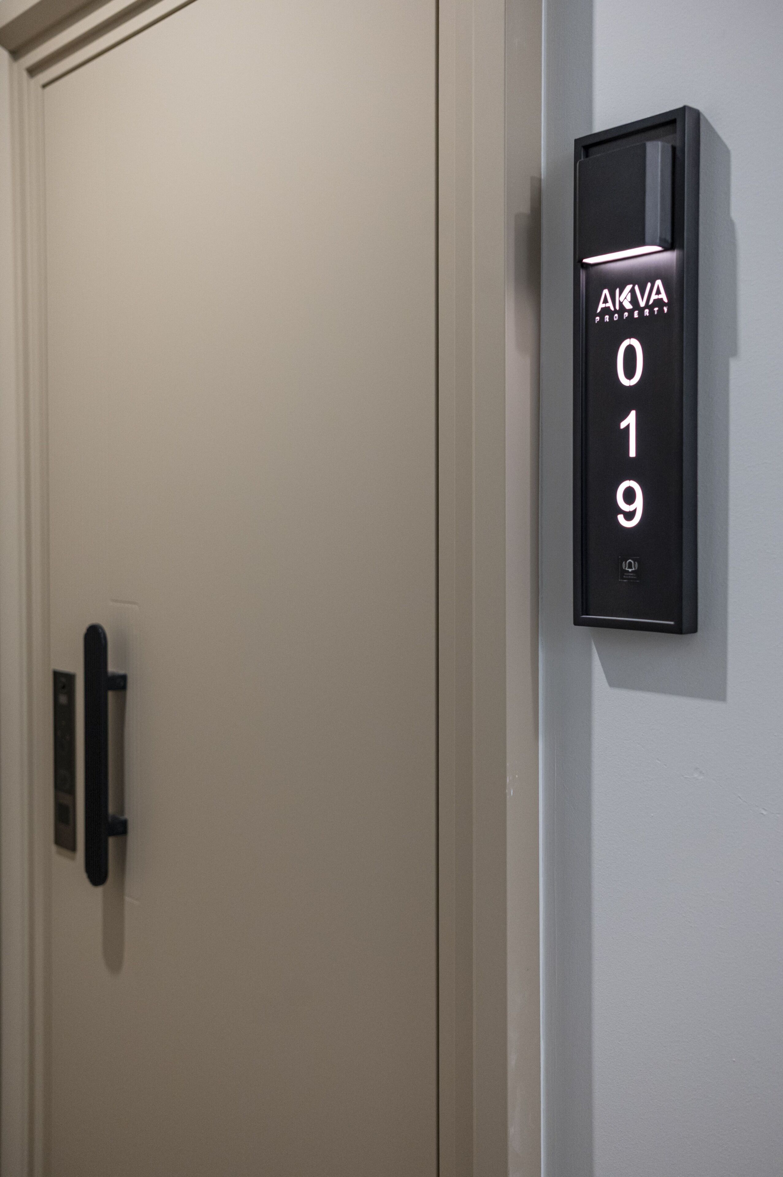 Eine Tür mit einer digitalen Anzeige, die die Nummer 019 zeigt, und eine schwarze Tafel mit dem Text 'AKVA PROPERTY'.