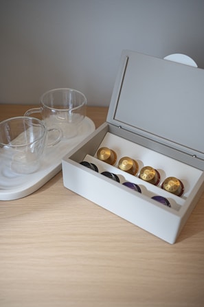 A white box with compartments containing capsules and two clear glass cups on a tray.