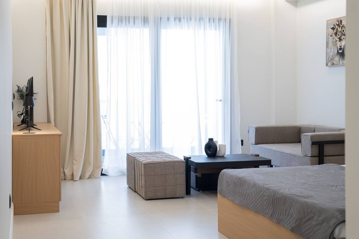 Moderni hotellihuone, jossa on sänky, sohva, työpöytä ja suuri ikkuna, jossa on verhot.