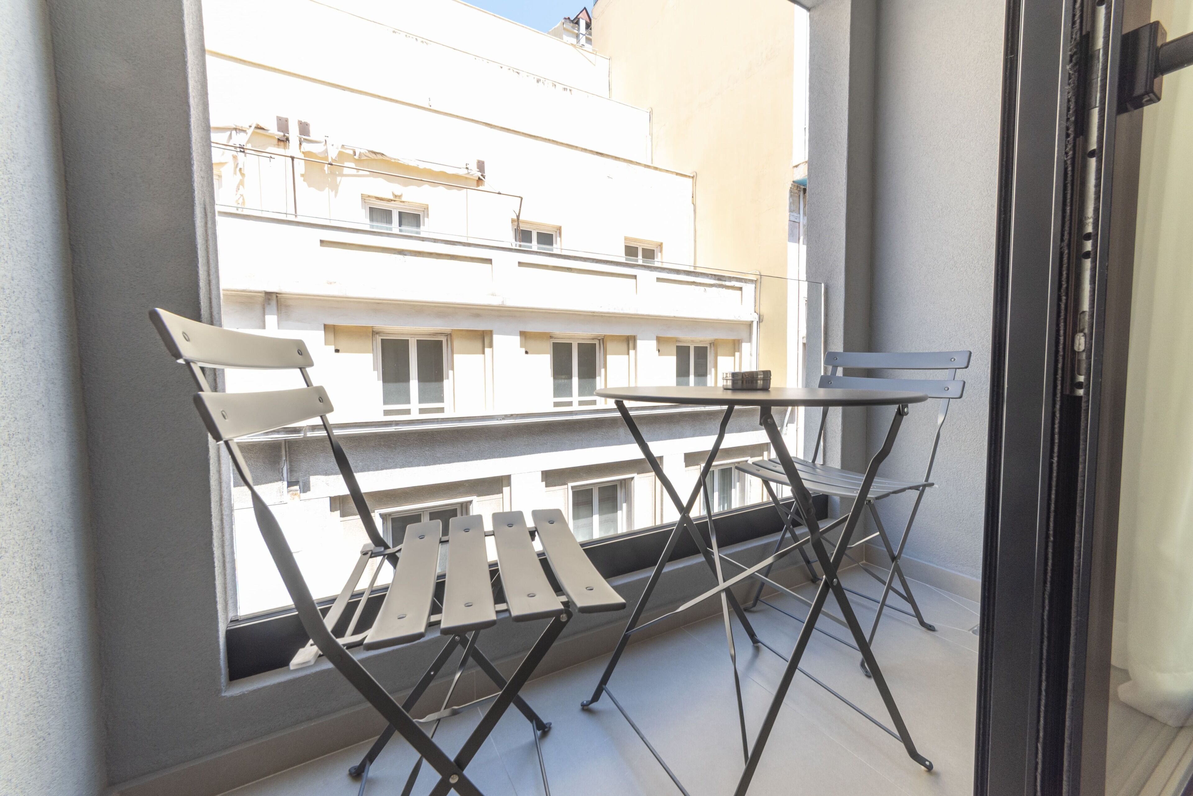 Un balcon avec une table et des chaises, une fenêtre et une vue sur un immeuble.
