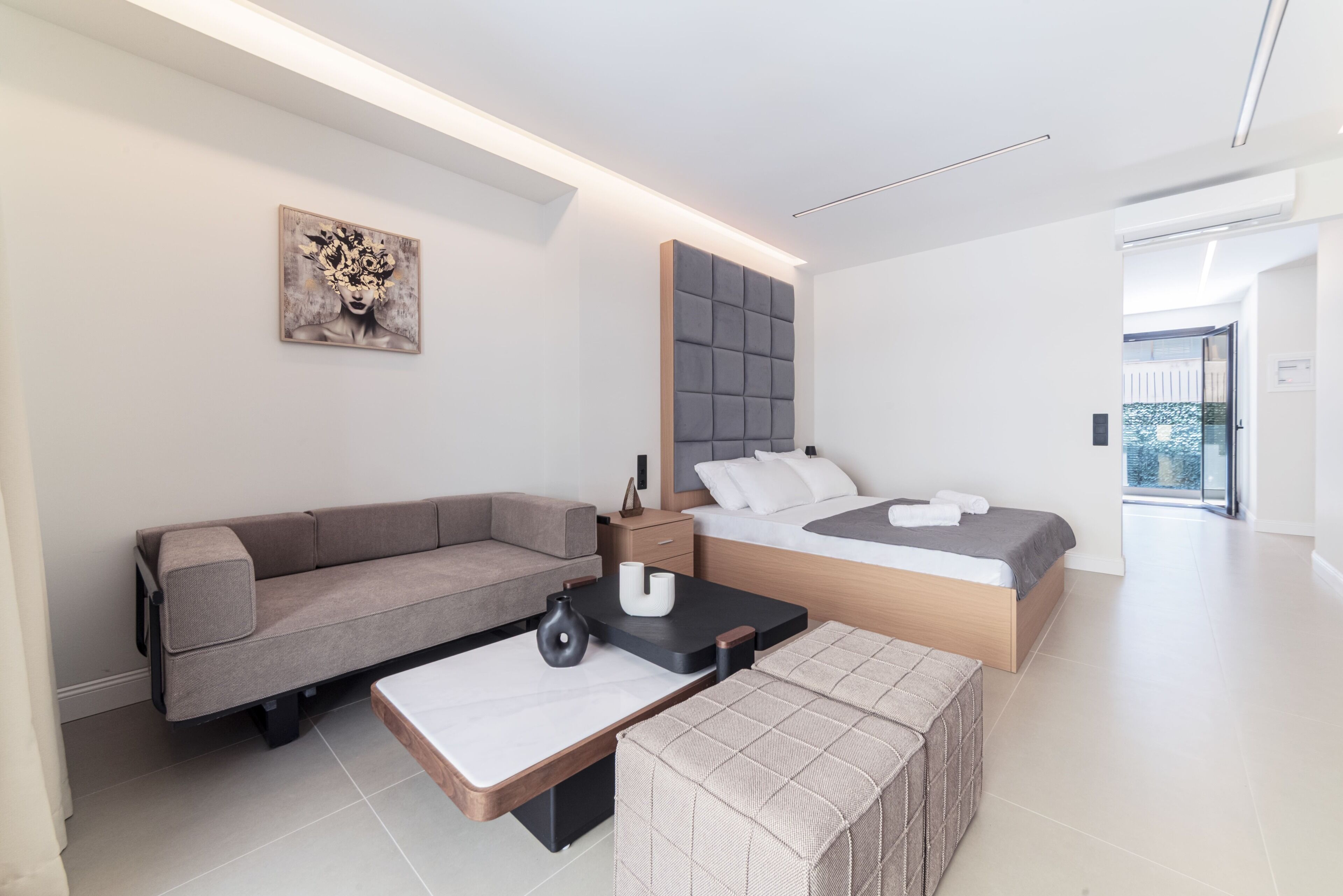 A modern bedroom with a sofa, a bed, a bedside table, and a painting on the wall.
