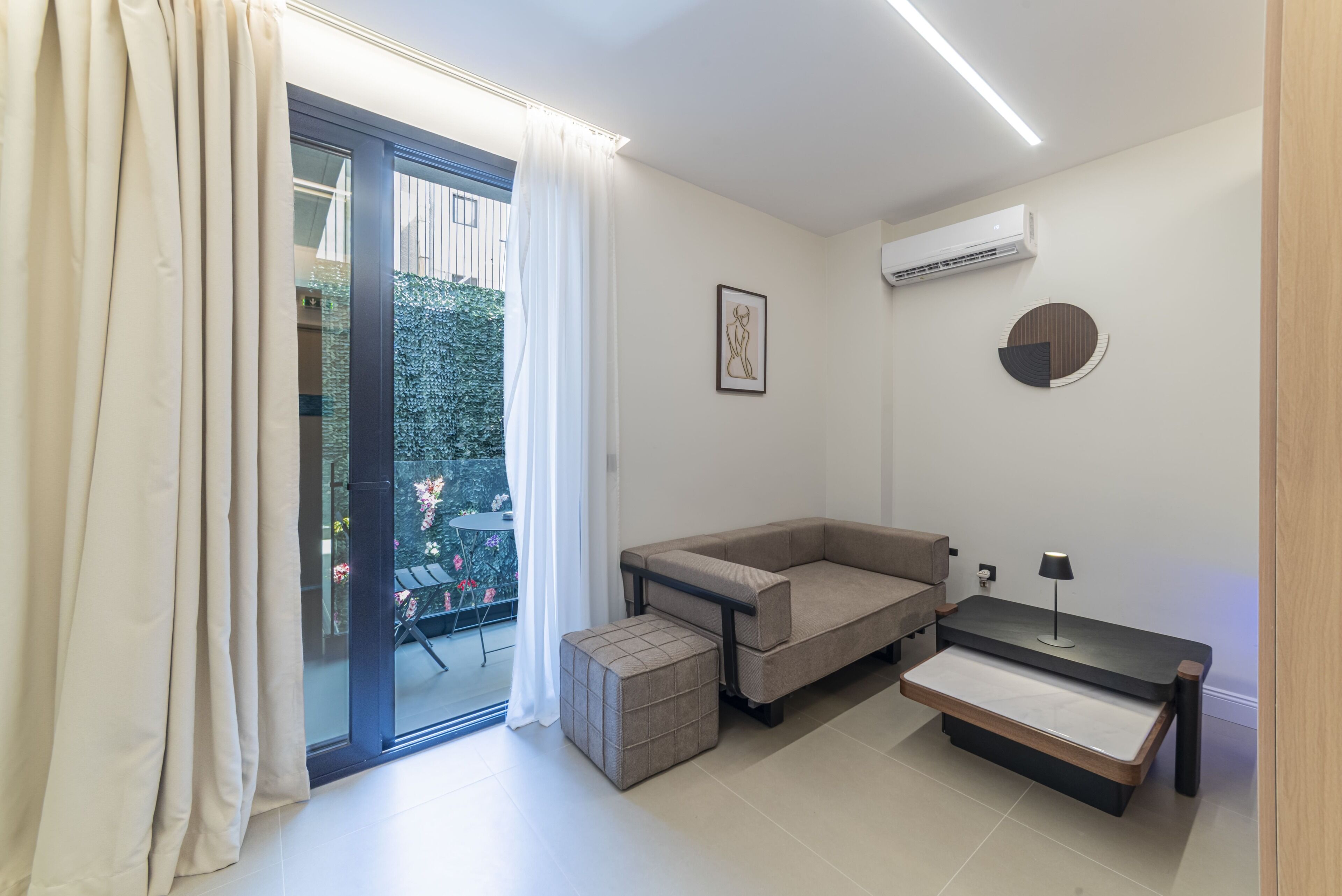 A modern room with a sofa, ottoman, and a small table with a lamp.