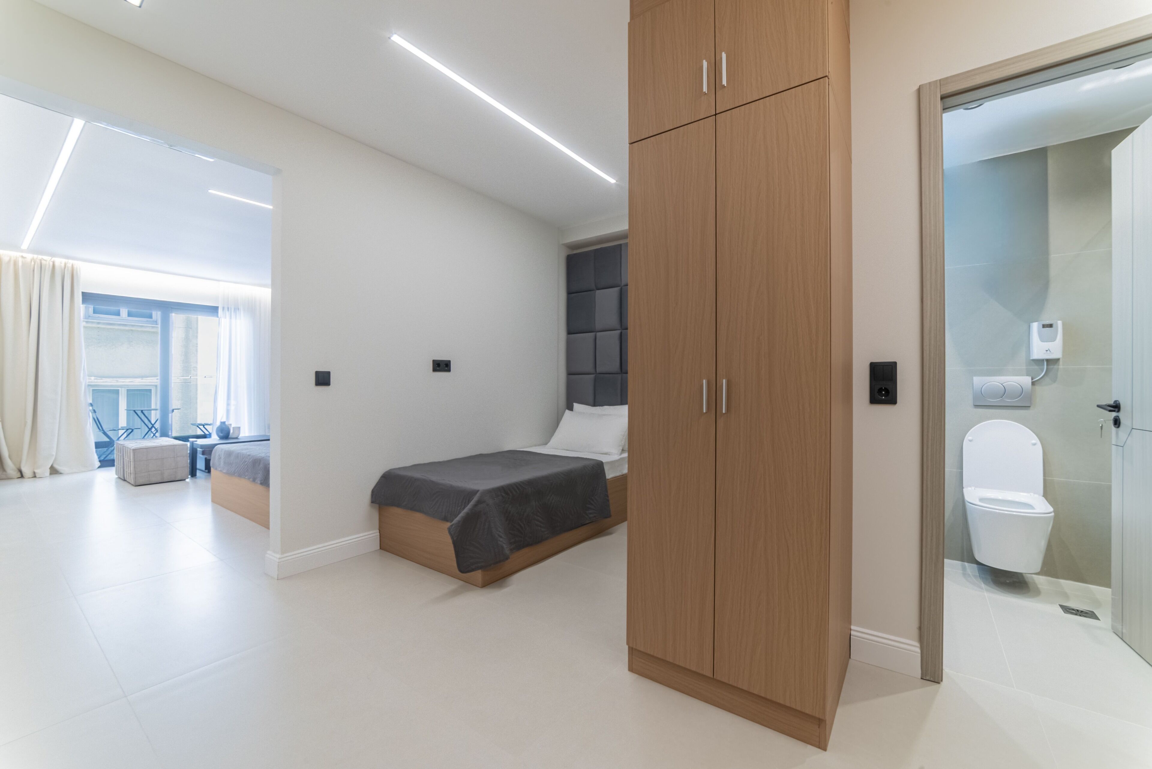 A modern bedroom with a bed, wardrobe, and a bathroom with a toilet and shower.