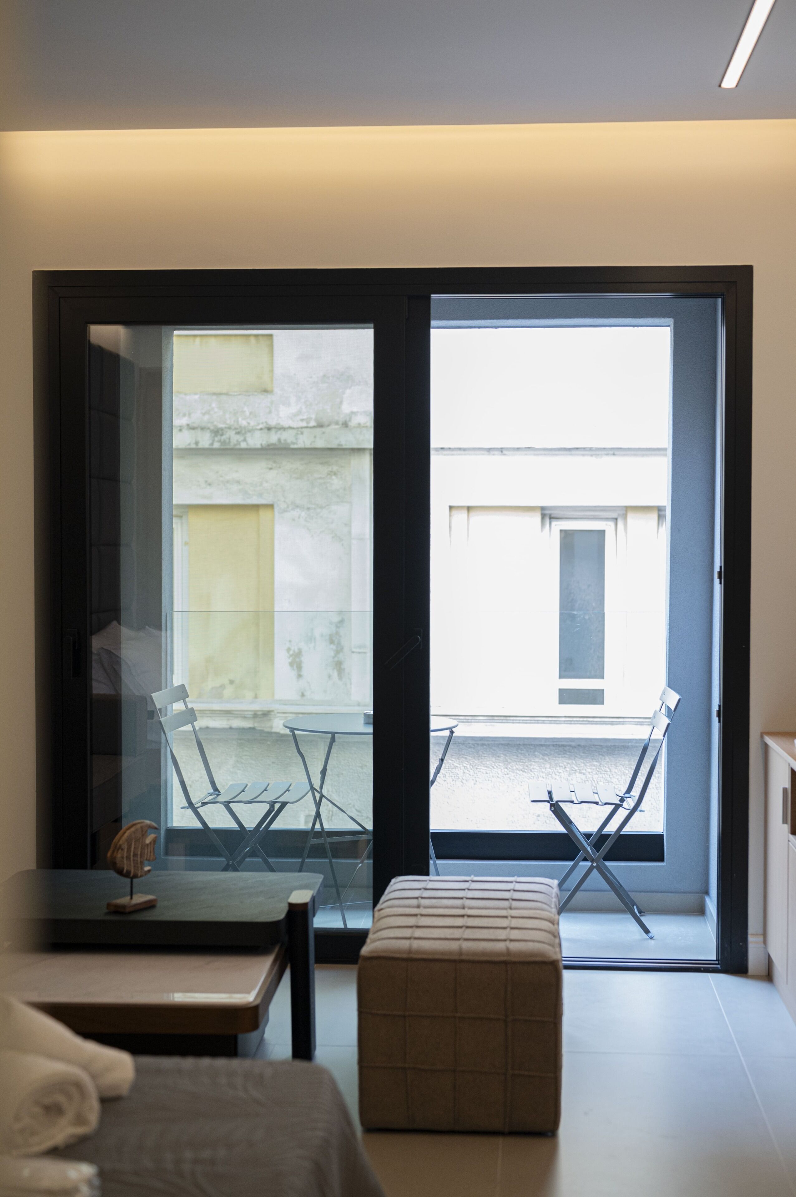 A modern room with a sliding glass door leading to an outdoor area, a small table with chairs, and a cushioned bench.