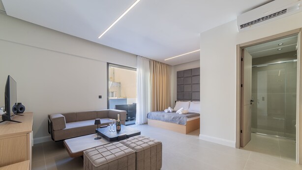 A modern hotel room with a sofa, a bed, a desk, and a glass shower enclosure.