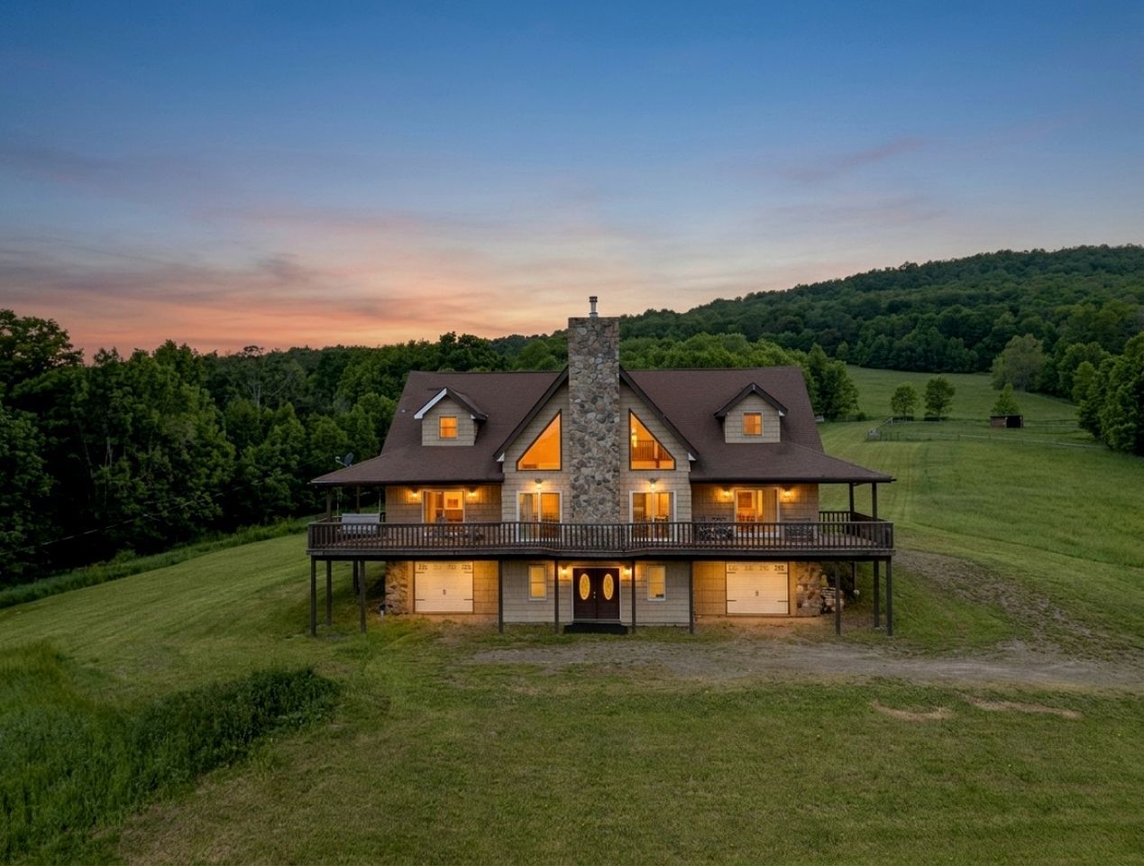 Une grande maison à deux étages, dotée d’une cheminée en pierre, de nombreuses fenêtres et d’un porche abrité.