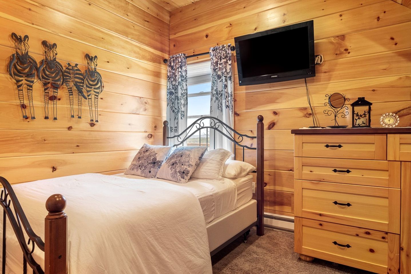 A wooden-paneled room with a bed, a TV, a dresser, and wall art.