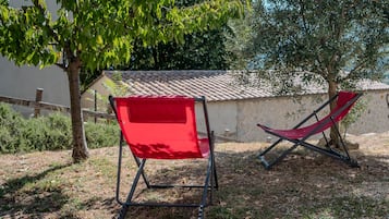 Duas cadeiras vermelhas dobráveis num jardim com uma estrutura de telhado em azulejos e uma parede de pedra ao fundo.