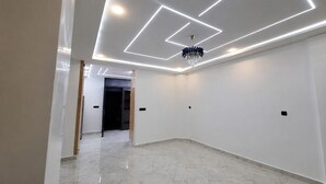 A modern interior with a hallway leading to a dark room, white walls, and a chandelier.