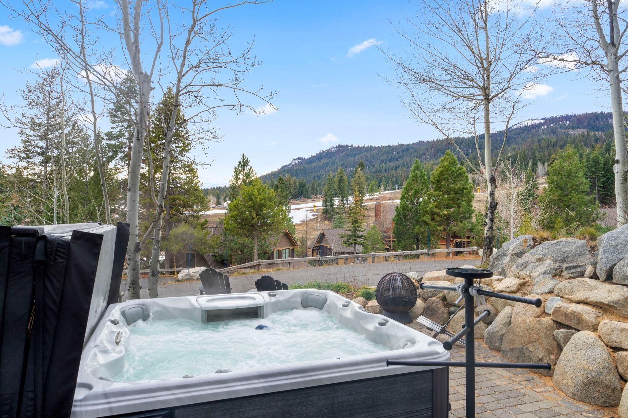 Ein Whirlpool mit Blick auf eine gebirgige Landschaft, eine Holzterrasse und eine Steinmauer.