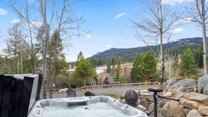 Ein Whirlpool mit Blick auf eine gebirgige Landschaft, eine Holzterrasse und eine Steinmauer.