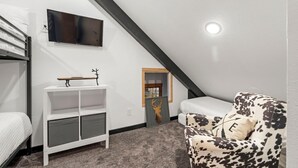 Ein Zimmer mit einem Etagenbett, einem Schreibtisch mit Stuhl, einer Couch und einem Fernseher an der Wand, sowie einem Fenster.