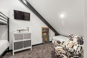 Ein Zimmer mit einem Etagenbett, einem Schreibtisch mit Stuhl, einer Couch und einem Fernseher an der Wand, sowie einem Fenster.