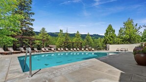 Ein Schwimmbecken mit Liegestühlen und einer Pergola, umgeben von Bäumen und Blick auf einen Berg.