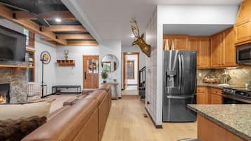 A modern kitchen with wooden cabinets, a stainless steel refrigerator, and a stone fireplace.