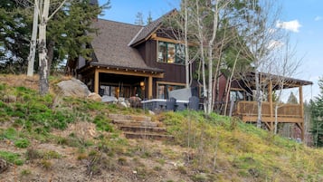 A two-story wooden house with a stone foundation, a deck, and a staircase leading to the entrance.