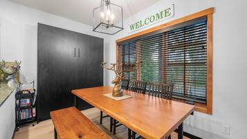 A dining area with a wooden table, benches, a deer sculpture, a 'WELCOME' sign, and a window with blinds.