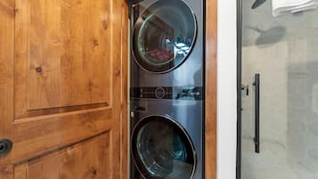 A laundry room with two front-loading washing machines, a wooden door, and a glass shower enclosure.