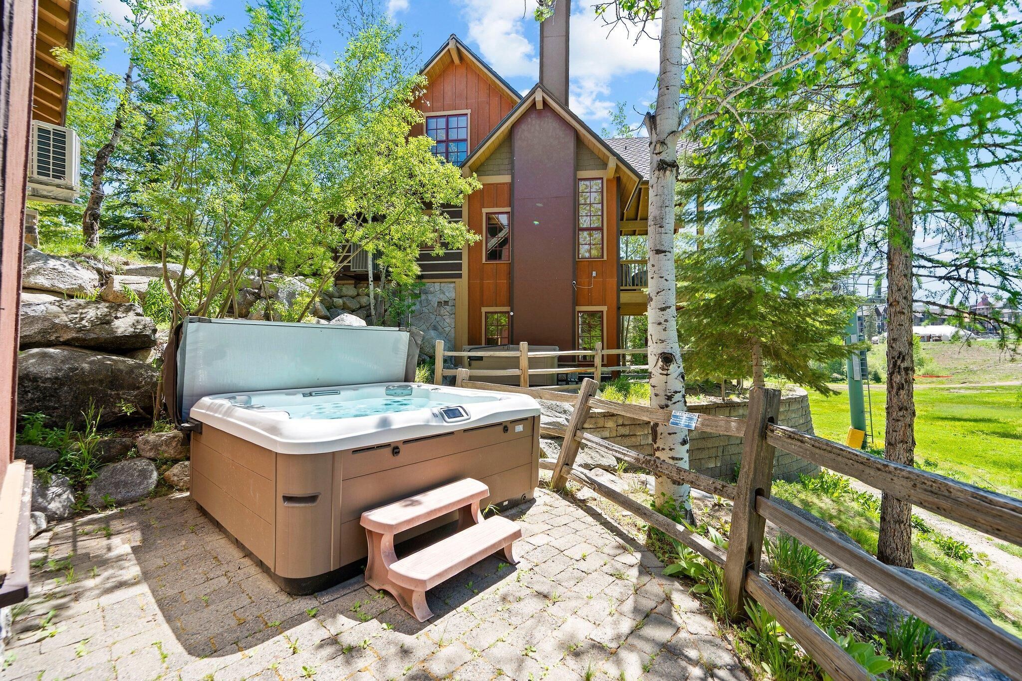 Un bain à remous avec des marches, situé dans un espace extérieur aménagé, agrémenté d’une clôture en bois et d’arbres.