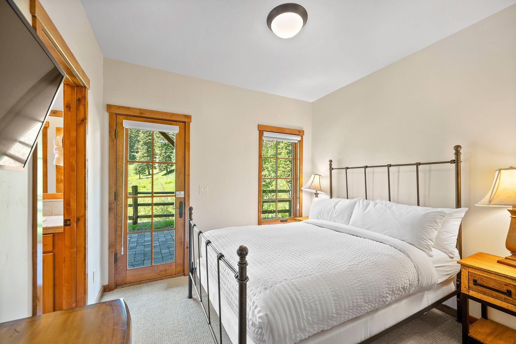 A bedroom with a large bed, wooden headboard, two windows, and a nightstand with a lamp.
