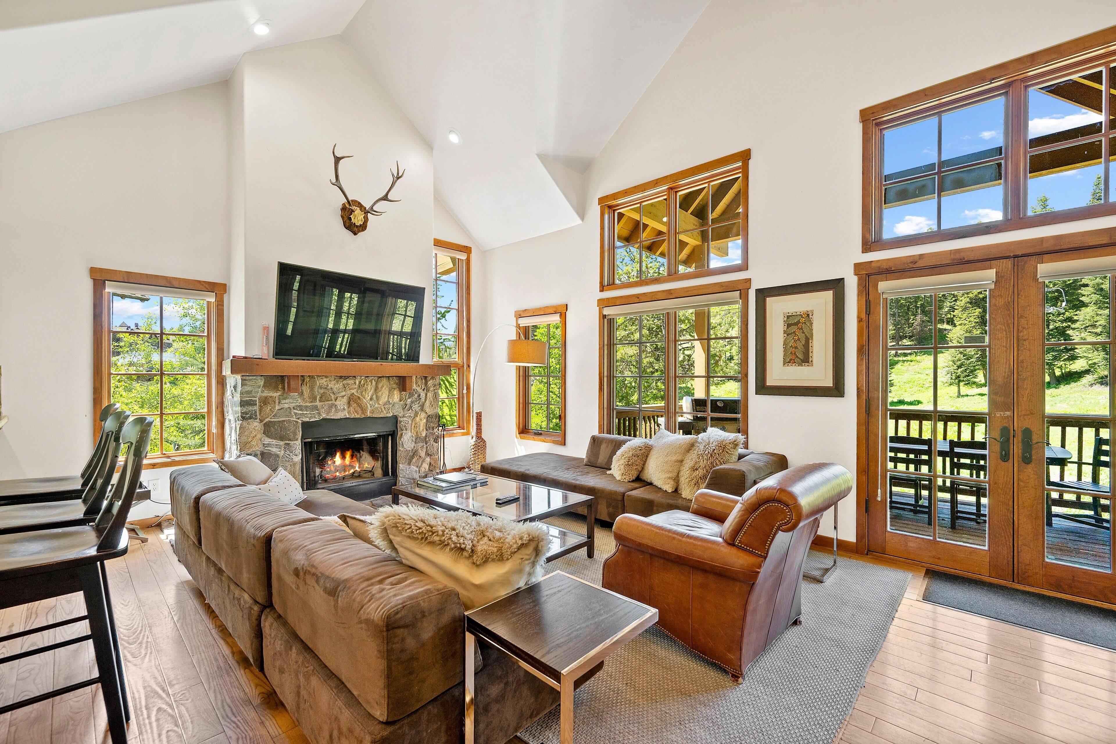 A spacious living room with a stone fireplace, comfortable seating, and large windows offering views of the outdoors.