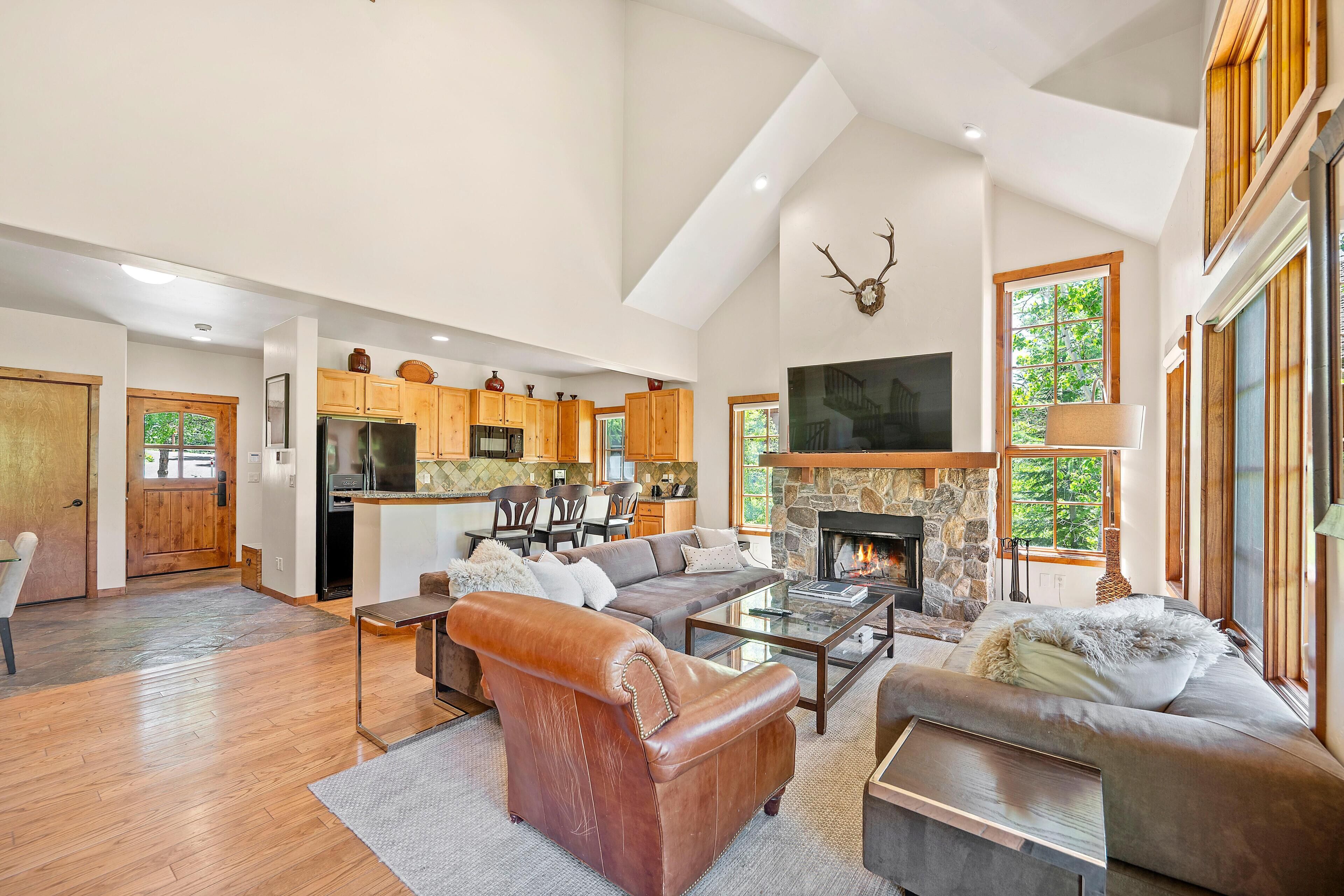A spacious living area with a fireplace, a kitchen with wooden cabinets, and a large window.