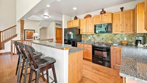 A kitchen with wooden cabinets, granite countertops, a refrigerator, stove, and bar stools. - Powderhound | Exclusive Tamarack Perks (Tamarack)