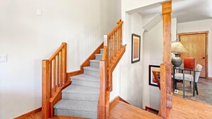 A staircase with wooden railings and carpeted steps leading to a dining area with a table and chairs. - Powderhound | Exclusive Tamarack Perks (Tamarack)